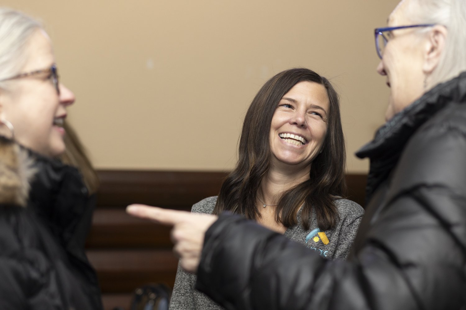 Three women smiling and talking, two wearing glasses, in a social setting.