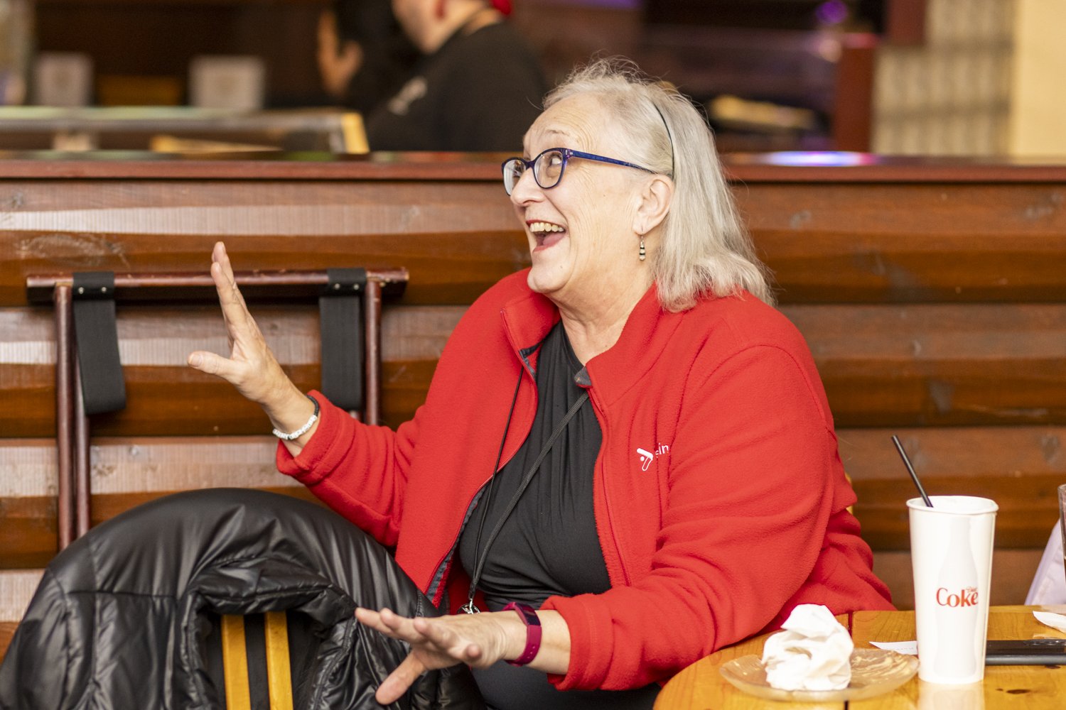 Smiling woman in a red jacket talking at a table in a restaurant.