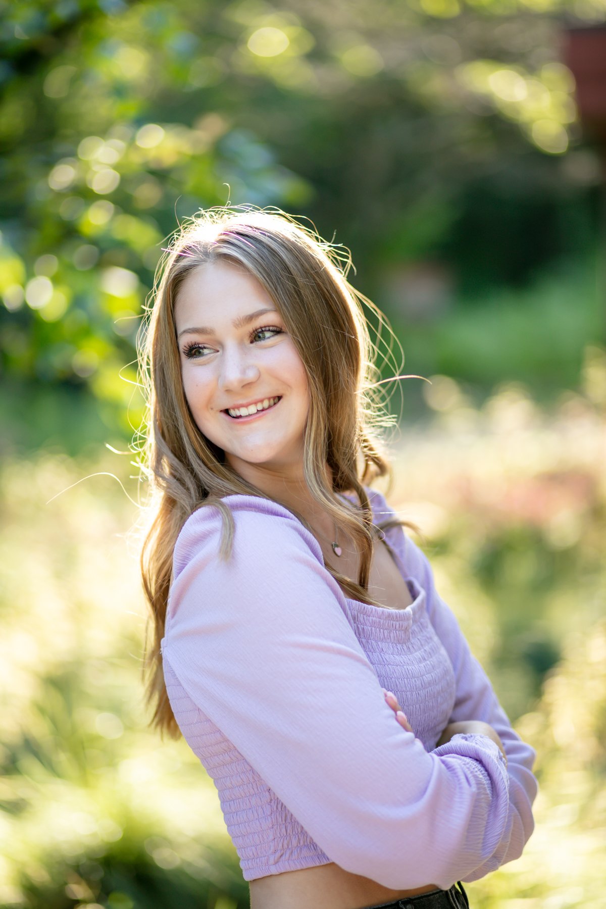 Smiling person in a light purple top standing outdoors with blurred green background.