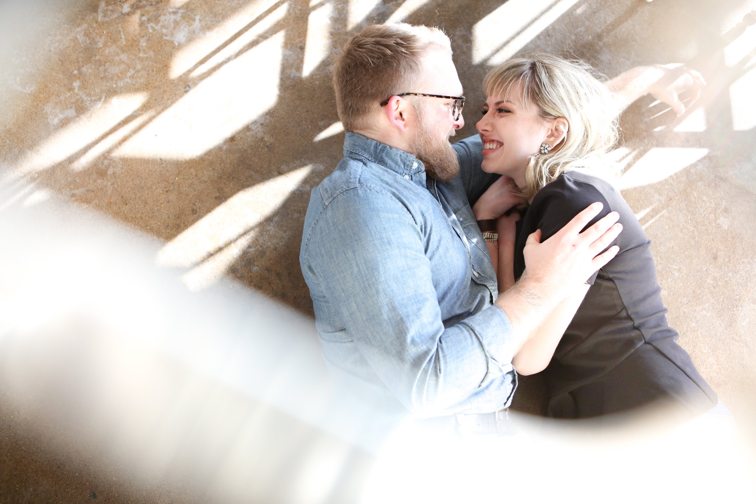 A couple lying on the floor, smiling at each other, with soft sunlight creating shadows around them.