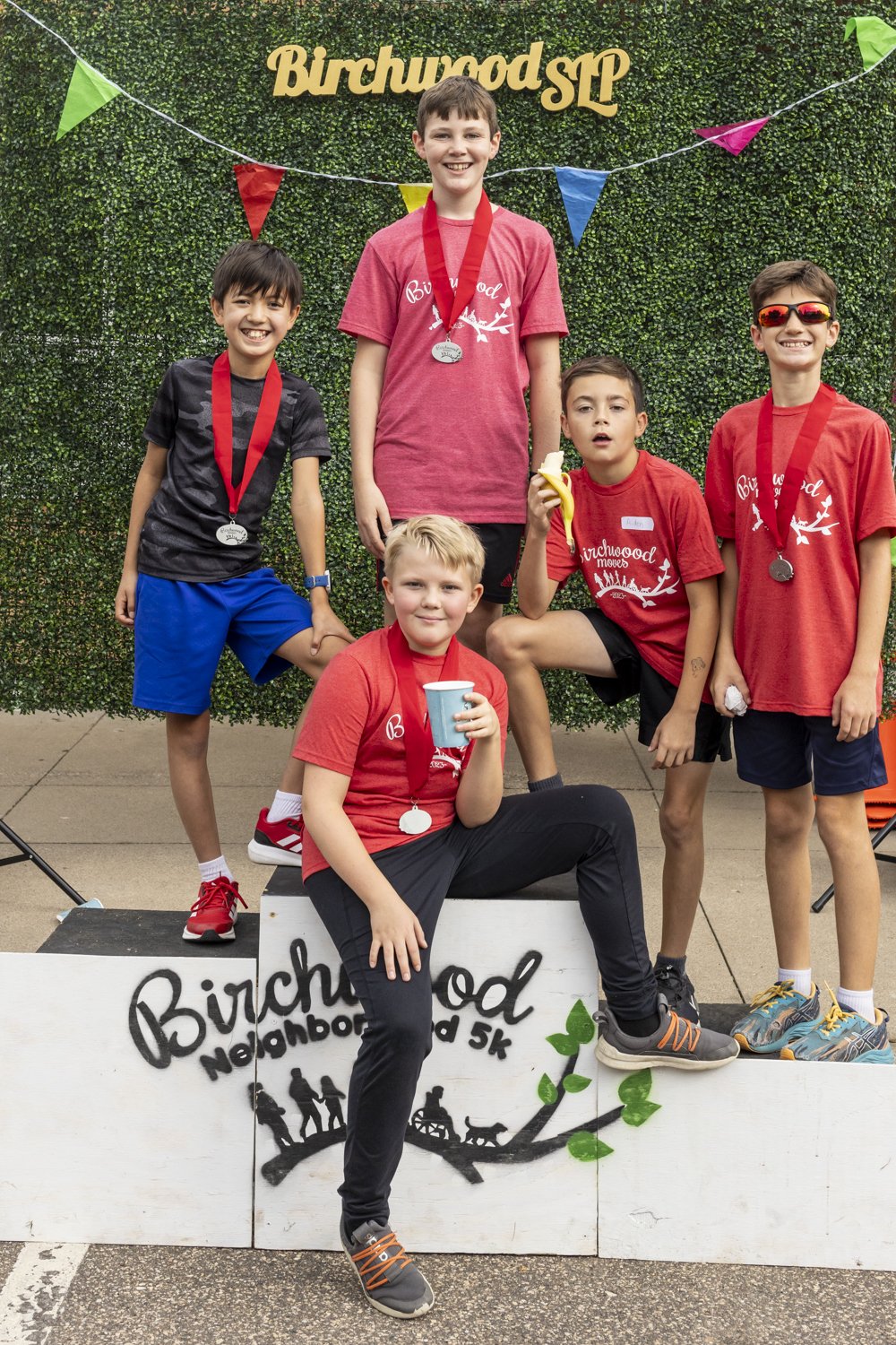 Group of five boys posing with medals after a 5k event, "Birchwood SLP" backdrop, wearing sports clothing.