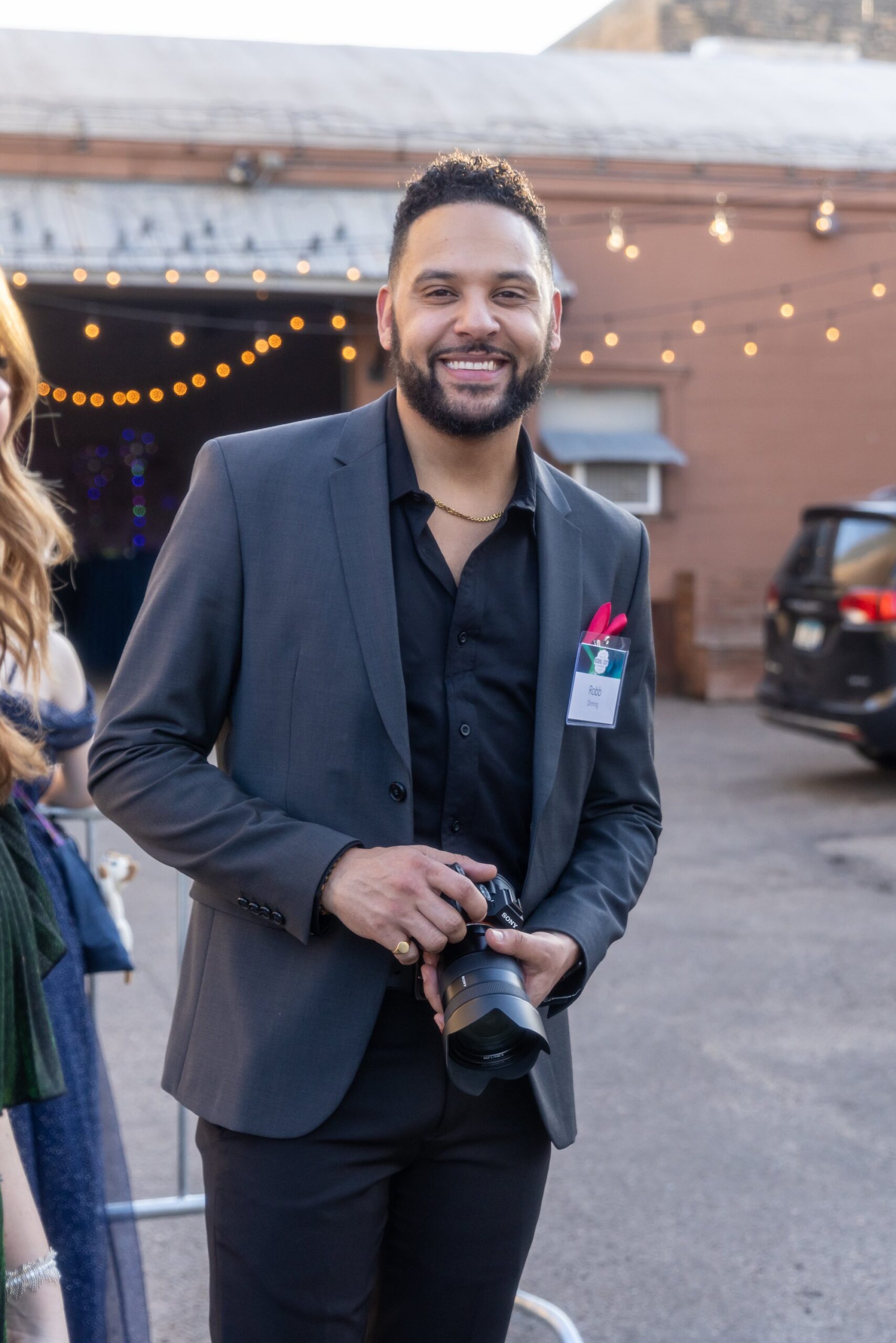 Man in a suit holding a camera at an outdoor event.