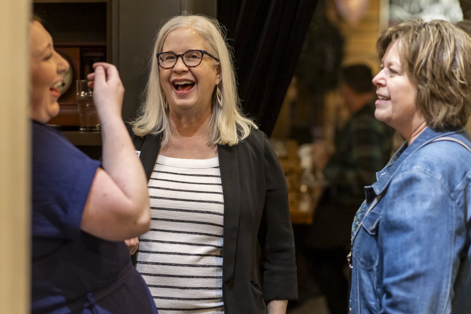 Three women laughing and talking in a social setting.