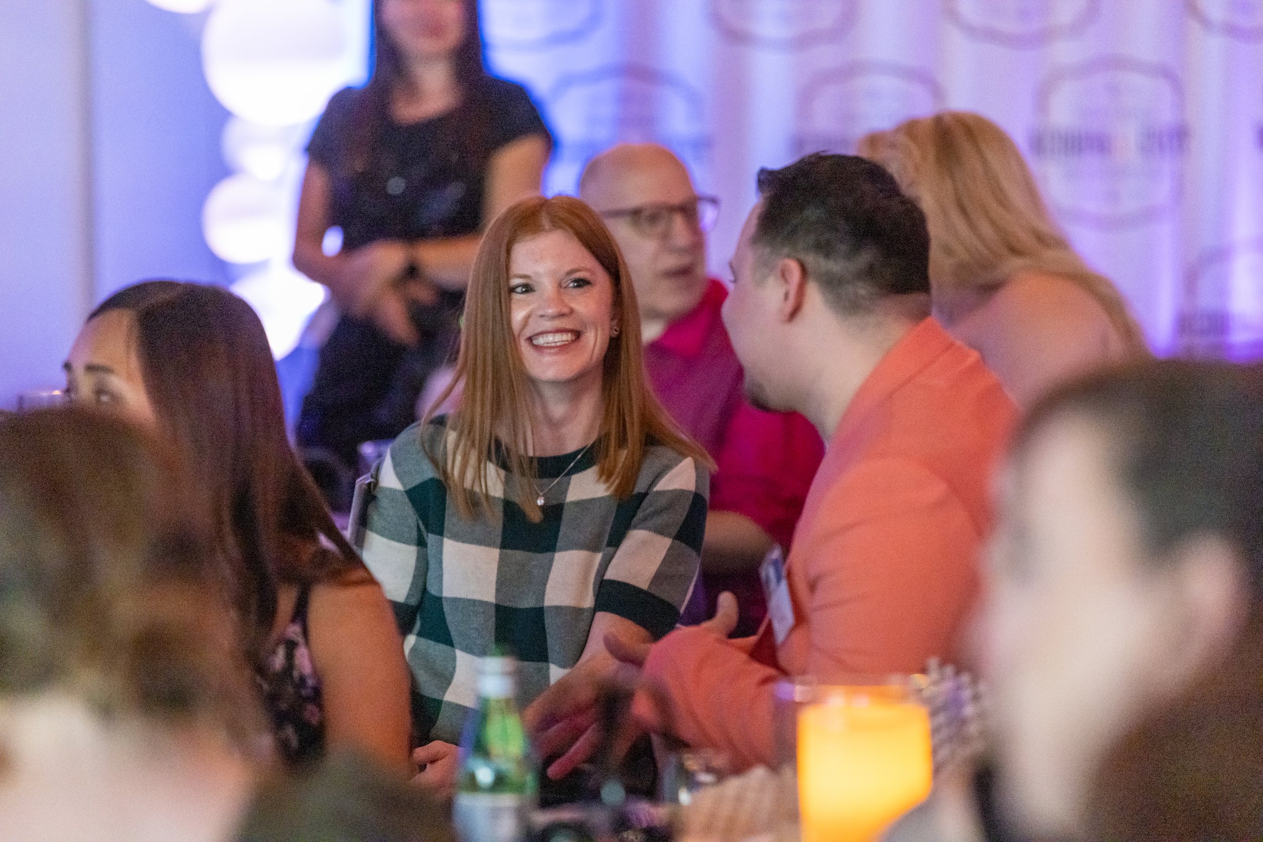 People sitting and talking at an event, smiling and engaged in conversation, with a blurred background.