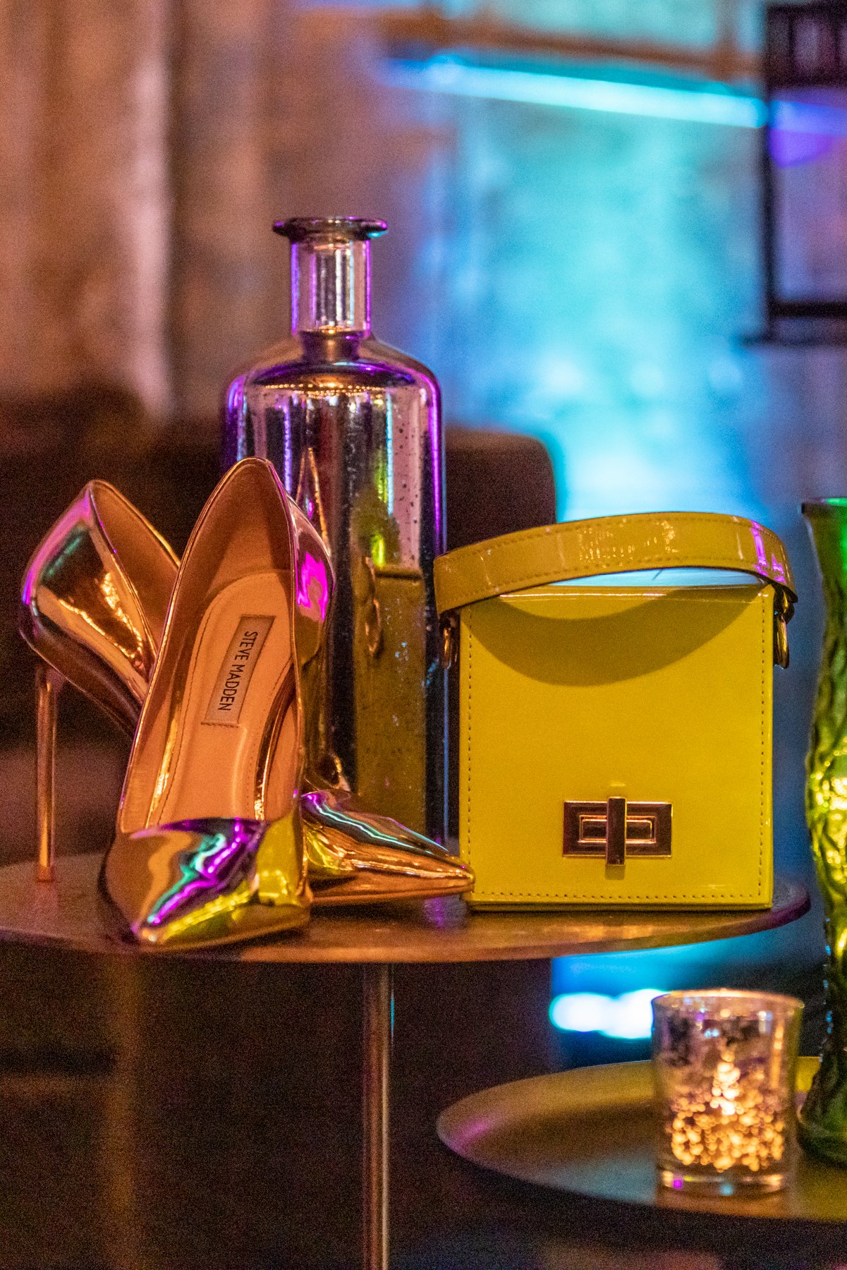 Metallic high heels, yellow handbag, glass bottle, colorful lighting