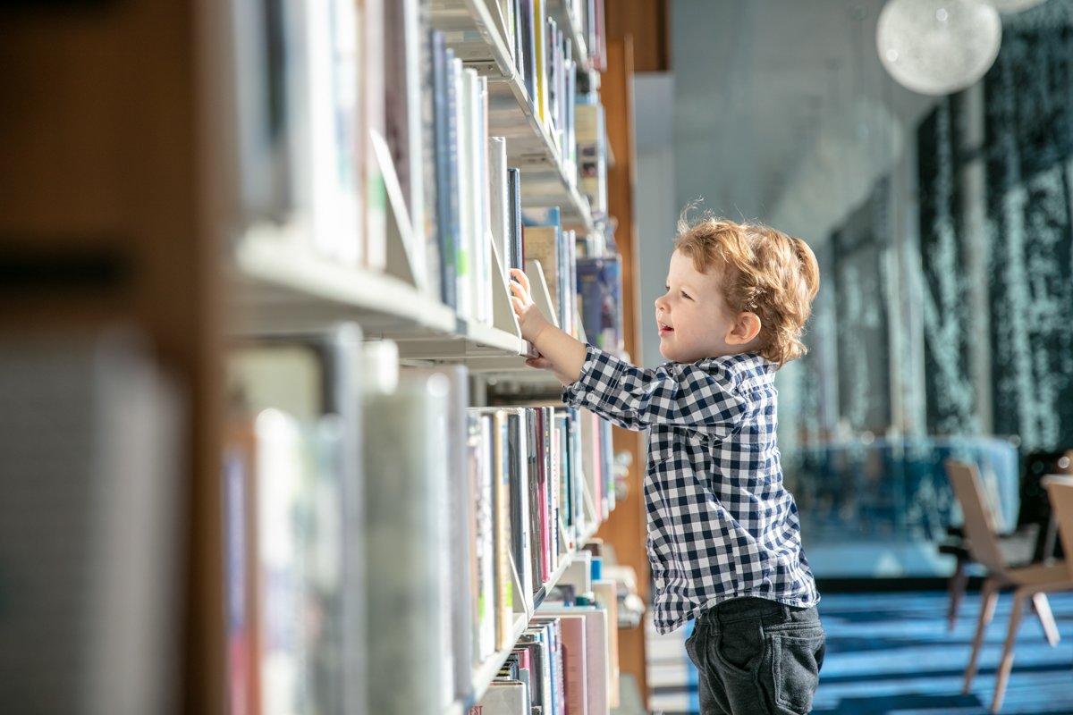 Child reaching for books on a library shelf.