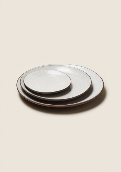 Stacked beige ceramic plates against a neutral background. Sizes vary from small to large.