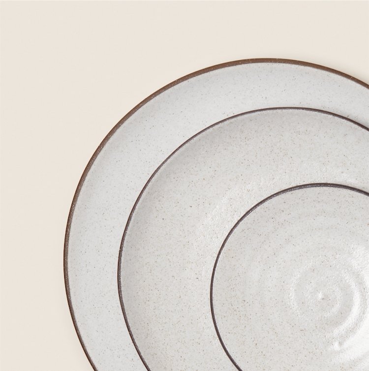 Stacked ceramic plates with a speckled finish on a light background.