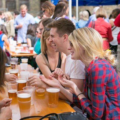 A group of people sitting at a long outdoor table with plastic cups of beer, talking and laughing.