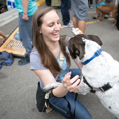 Woman smiling and playing with a dog at an outdoor event.