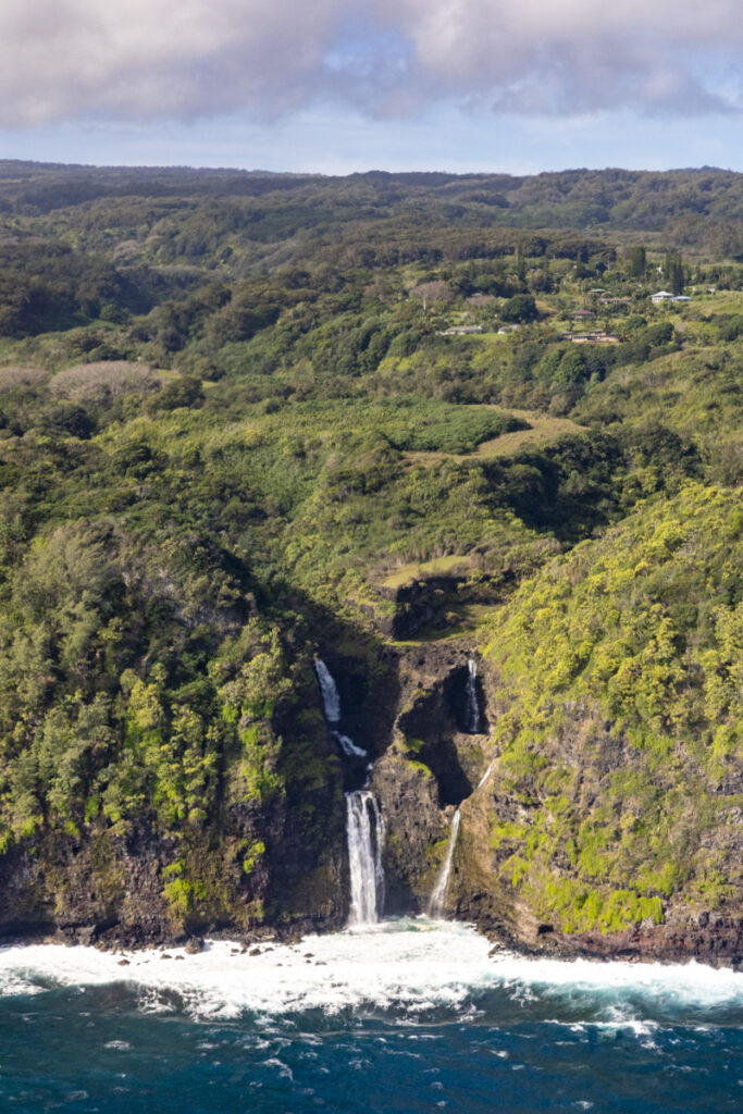 Waterfall cascading through deep rainforest valley seen from helicopter window Hana Maui
